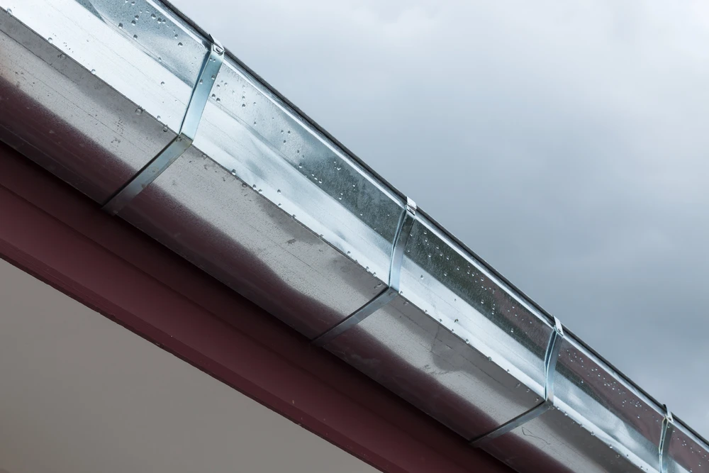 Ouvrier installant une gouttière sur le toit d'une maison résidentielle à bardage bois