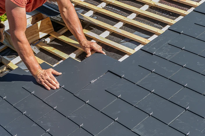 Chantier de toiture en cours avec ouvrier installant des tuiles plates grises sur charpente à structure métallique rouge