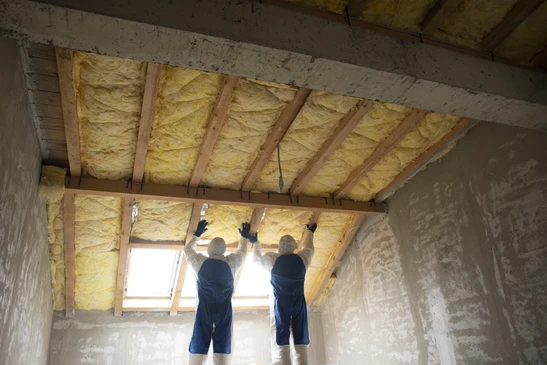 Ouvrier en gilet haute visibilité jaune découpe un panneau d'isolant thermique avec un couteau à lame rétractable sur un chantier de construction